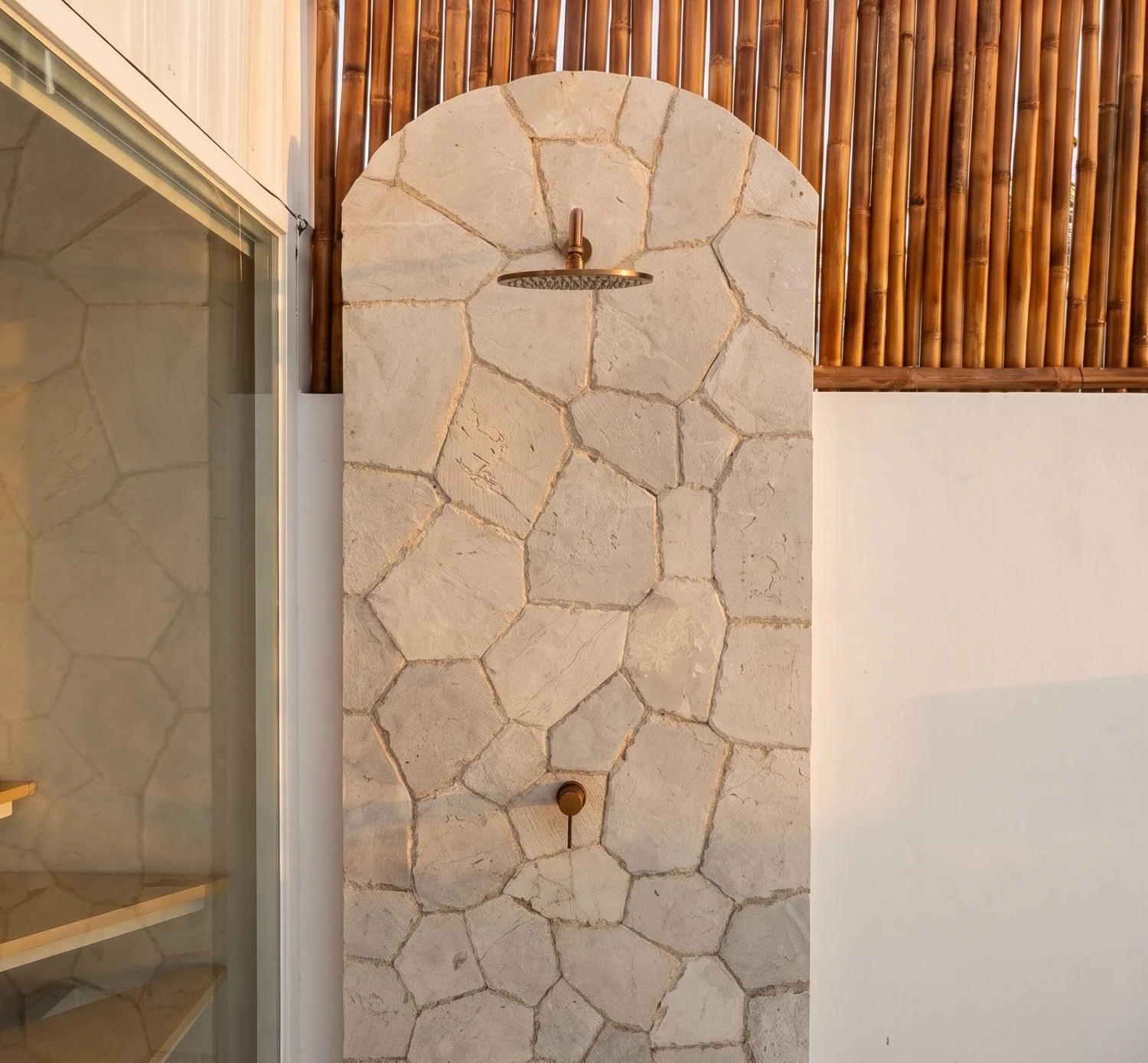Stone-clad archway shower with a copper rain shower head, framed by bamboo fencing and the staircase beyond at Villa Mares